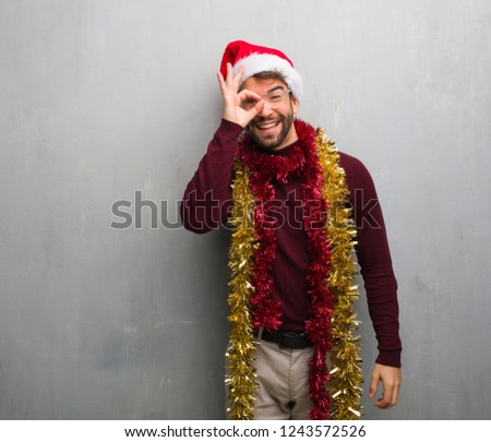 Young man celebrating christmas day holding gifts confident doing ok gesture on eye