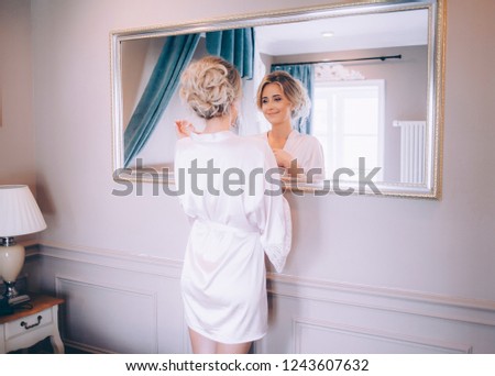 Bride examines in the mirror the makeup and hairstyle that the makeup artist did