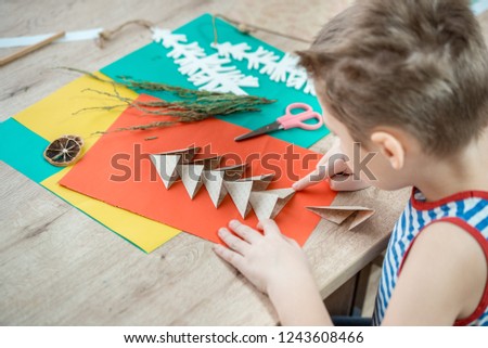 Child's hands cutting colored red paper with scissors . Christmas tree made of colored paper. cute boy doing crafts