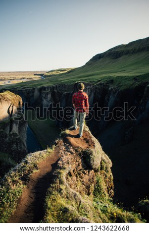 Vertical for story social media photo of young man in hiking pants and red checkered shirt stand on edge of cliff or end of trail head overlook epic landscape, mesmerized by nature beauty