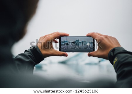 Big screen and high resolution futuristic, immersive technology smartphone, man makes photo or video of beautiful nordic landscape, ice cold ocean with floating icebergs and glaciers