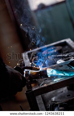Male worker wearing protective gloves while repairing car exhaust pipe with welding machine