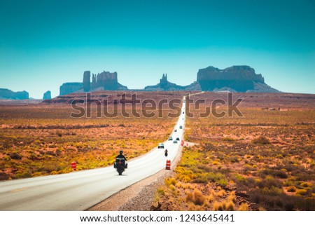 Classic panorama view of motorcyclist on historic U.S. Route 163 running through famous Monument Valley in beautiful golden evening light at sunset in summer, Utah, USA Royalty-Free Stock Photo #1243645441