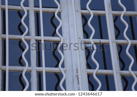 Close up outdoor view of a white wooden window with rectangular glasses protected by steel bars. Abstract image with curving lines and rectangles. Graphic picture of an object.