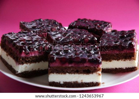Pieces of chocolate cheese cake with blackcurrant filling / topping on a round plate. Close-up of sweet dessert against pink / light magenta background. 