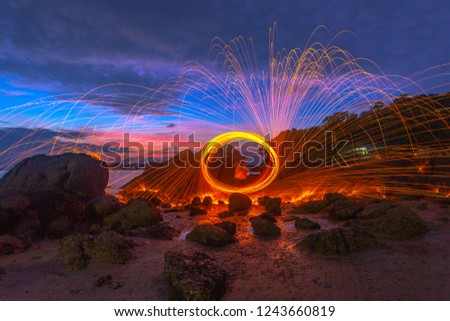 reflection of spark fire swirl from steel wool with long exposure speed motion abstract at sunrise in the sea
