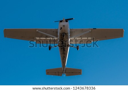 A small single engine airplane directly overhead. Blue sky above. Fast shutter to freeze propeller. Bottom of plane is dirty.