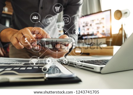 Businessman hand working digital marketing media in virtual screen with mobile phone and modern compute with VR icon diagram at office in morning light 