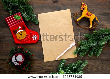 New Year or Christmas mockup. Template for letter to Santa, list of plans and goals for New Year, wishlist near fir branches, Christmas socks, toy horse on dark wooden background top view