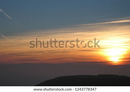 Colorful abstract sunset with horizontal clouds and color display, blue sky and airplane condensation stripes