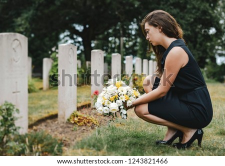 Young widow laying flowers at the grave Royalty-Free Stock Photo #1243821466