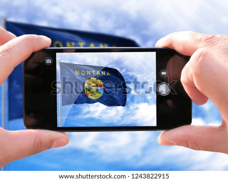 The hands of men make a phone photograph of the flag State of Montana.