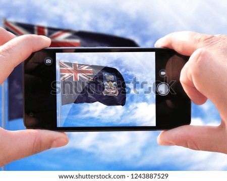The hands of men make a phone photograph of the flag of Falkland Islands