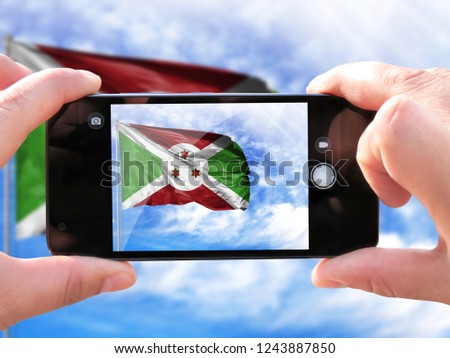 The hands of men make a phone photograph of the flag of Burundi