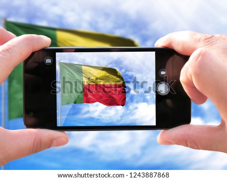 The hands of men make a phone photograph of the flag of Benin