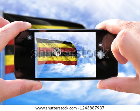 The hands of men make a phone photograph of the flag of Uganda