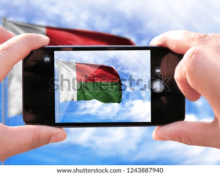 The hands of men make a phone photograph of the flag of Madagascar