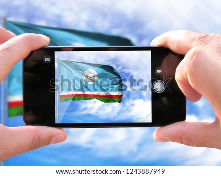 The hands of men make a phone photograph of the flag of Sakha Republic