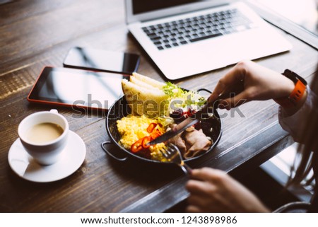 Business woman sitting with a laptop in a cafe and eating breakfast with a cup of coffee on the table.