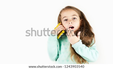 Bright beautiful little girl in headphones with the phone is emotionally surprised on an isolated background.