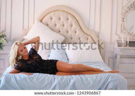 Beautiful adult plus size blonde woman having rest and comfort in her white bedroom with blue bed linen