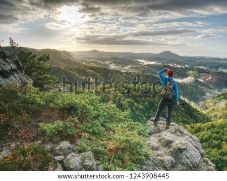 Freelancer create nature photos. Professional photographer takes photos with camera on tripod on rocky peak. Dreamy fogy landscape
