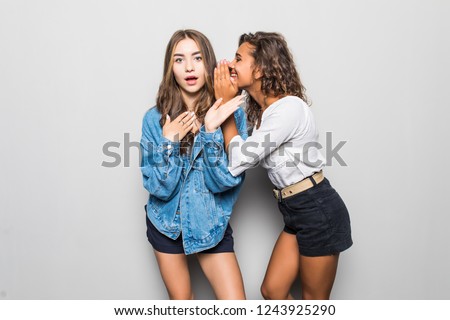 Portrait of two cute girls whispering a secret isolated over gray background