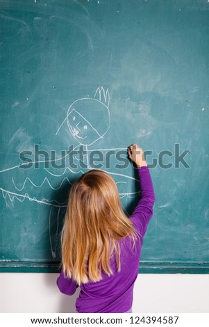 Studio portrait of young girl in classroom drawing image of girl in dress on a chalkboard