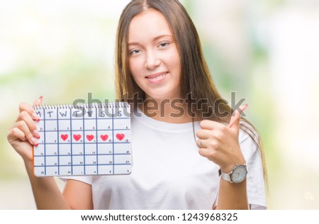 Young caucasian woman holding menstruation calendar over isolated background happy with big smile doing ok sign, thumb up with fingers, excellent sign