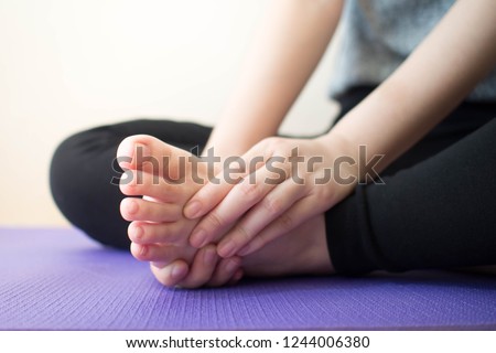 Foot pain - Young female massaging her painful foot after sport workout indoors while sitting on stretching mat. Health care concept. Close up. Royalty-Free Stock Photo #1244006380
