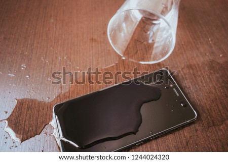 Smartphone wet by accident on wooden table. Glass of water spill