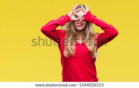 Young beautiful blonde woman wearing red sweater over isolated background doing ok gesture like binoculars sticking tongue out, eyes looking through fingers. Crazy expression.