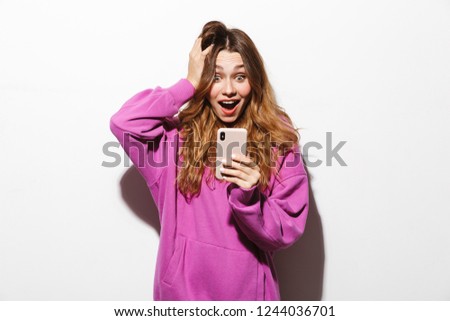 Portrait of joyous woman 20s wearing sweatshirt using smartphone while standing isolated over white background