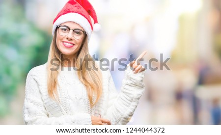 Young beautiful woman wearing christmas hat over isolated background with a big smile on face, pointing with hand and finger to the side looking at the camera.