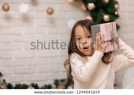 Pretty smiling girl holding Christmas gift in hand at home