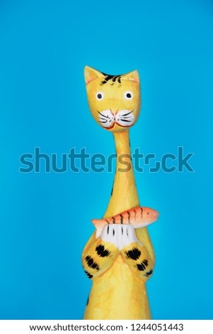 yellow wooden cat souvenir holds an orange fish in its paws 
