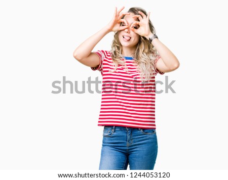 Beautiful young blonde woman over isolated background doing ok gesture like binoculars sticking tongue out, eyes looking through fingers. Crazy expression.