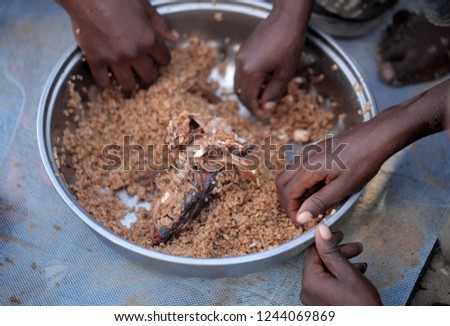 traditional african food: horizontal photography of a silver bowl full of rice dish, with black kids hands eating, outdoors on a sunny day in the Gambia, Africa