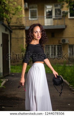 Beautiful casual ethnic woman with curly hair walking in the city, long white dress and black shirt