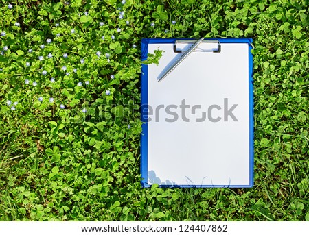 Blue medical clipboard with a pen over lush green clover grass