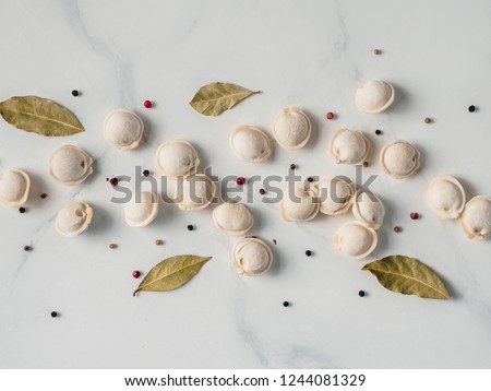 Pattern of frozen uncooked russian pelmeni with peppercorns and bay leaves on white marble table. Creative layout of dumplings. Beautiful scattered raw dumplings. Top view or flat lay.