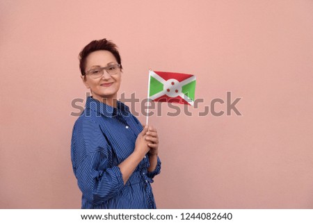 Burundi flag. Business woman holding flag. Nice portrait of middle aged lady 40 45 years old with a national flag over pink wall on the city street outdoors.