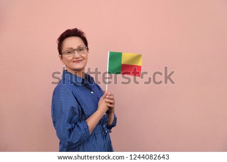Benin flag. Business woman holding Benin flag. Nice portrait of middle aged lady 40 45 years old with a national flag over pink wall on the city street outdoors.