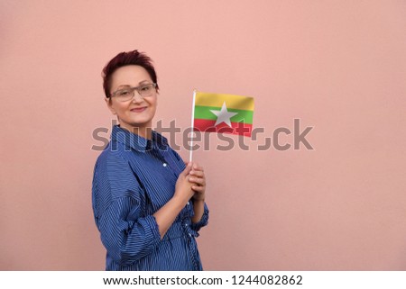 Myanmar flag. Business woman holding flag. Nice portrait of middle aged lady 40 45 years old with a national flag over pink wall on the city street outdoors.