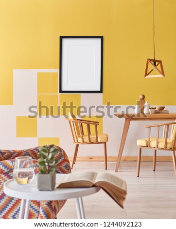 Picture and frame on the yellow wall and vertical room style with wooden table and chair, armchair and white coffee table interior.