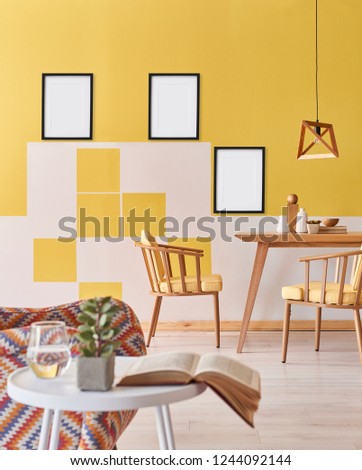 Picture and frame on the yellow wall and vertical room style with wooden table and chair, armchair and white coffee table interior.