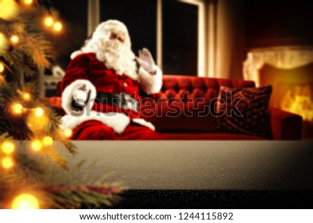 Table background with christmas tree and fireplace and red old santa claus on red sofa. 