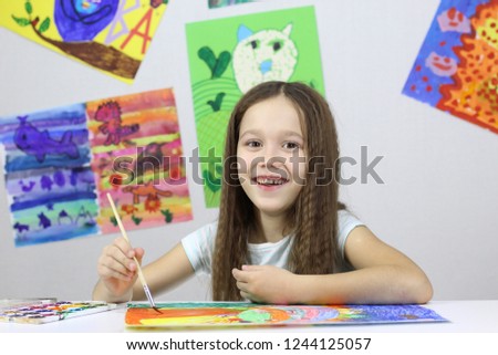 little girl draws a watercolor drawing on the background of a lot of drawings