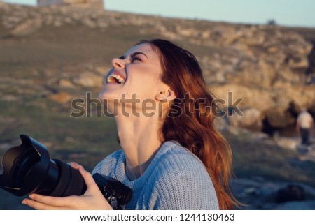 Happy woman on nature in the mountains holds a camera in her hands                          