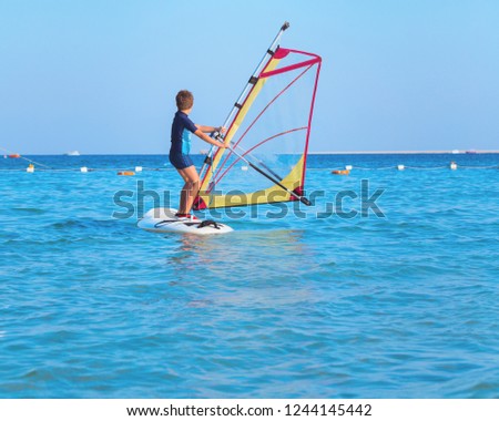 One child learning to windsurf in the sea at beautiful sunset light, close up, windsurfing passtime and school with copy space Royalty-Free Stock Photo #1244145442